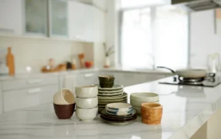 Various ceramic bowls and plates are neatly arranged on a countertop in a bright and airy kitchen.