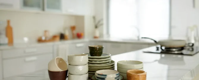 Various ceramic bowls and plates are neatly arranged on a countertop in a bright and airy kitchen.