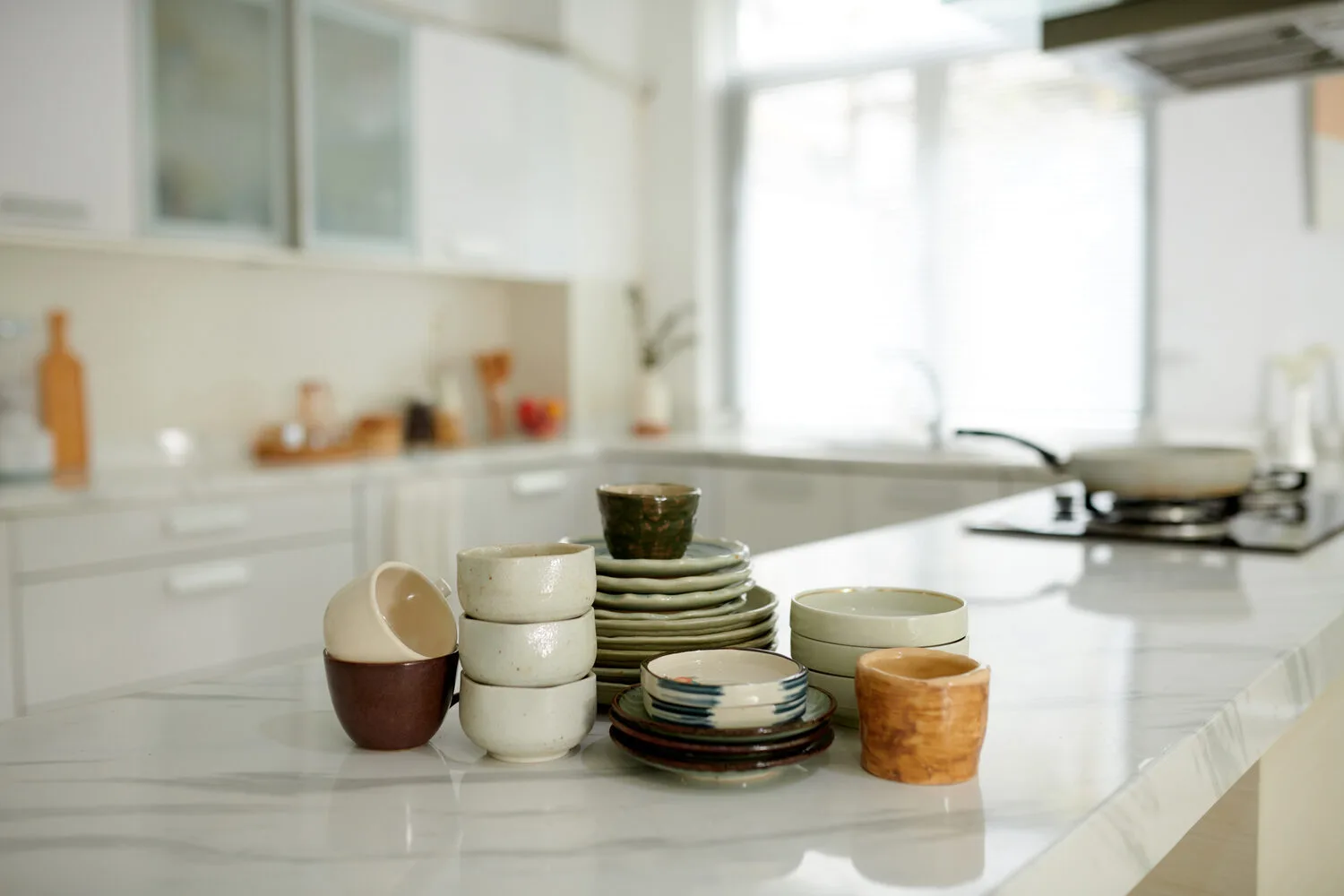 Various ceramic bowls and plates are neatly arranged on a countertop in a bright and airy kitchen.