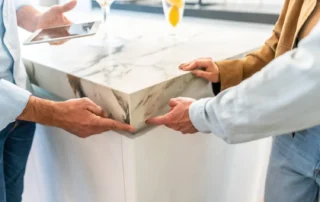 Three colleagues are gathered around a sleek marble countertop in a bright, modern kitchen setting.