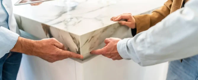 Three colleagues are gathered around a sleek marble countertop in a bright, modern kitchen setting.